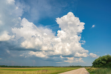 Large towering white cumulus clouds against a vivid blue summer sky above green and golden agricultural fields © Orbs production