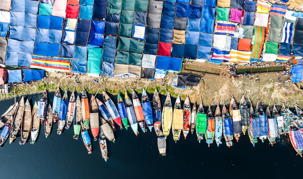 Aerial view of colorful boats docked along the riverbank at the Tongi river port, with rows of vibrant tarps and tents covering the area in Tongi, Dhaka Division, Bangladesh.