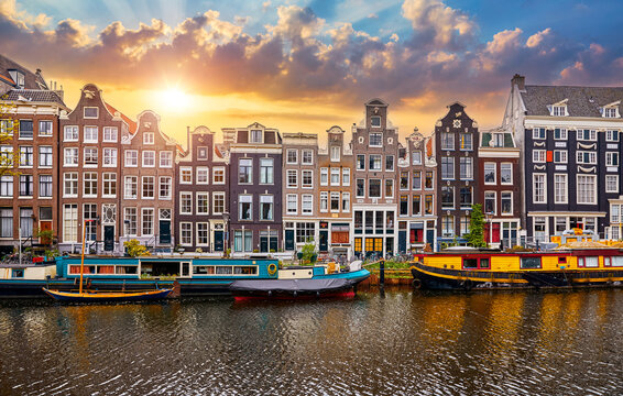 Amsterdam, Netherlands. Panorama of famous dancing houses on river Amstel, water channels with house boats. Popular landmark and travel destination in old european city. Evening sunset landscape.