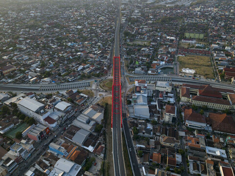 Aerial view of the Joglo Railway Bridge, a red steel structure spanning over the dense urban landscape with surrounding rooftops in Kecamatan Banjarsari, Jawa Tengah, Indonesia.