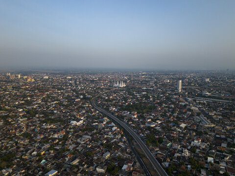 Aerial view of the Joglo Railway Bridge spanning across the dense urban landscape of the city with residential rooftops and clear sky in Kecamatan Banjarsari, Jawa Tengah, Indonesia.