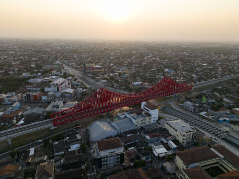 Aerial view of Joglo Railway Bridge, a striking red steel structure spanning over the dense urban landscape of Kecamatan Banjarsari, Jawa Tengah, Indonesia.