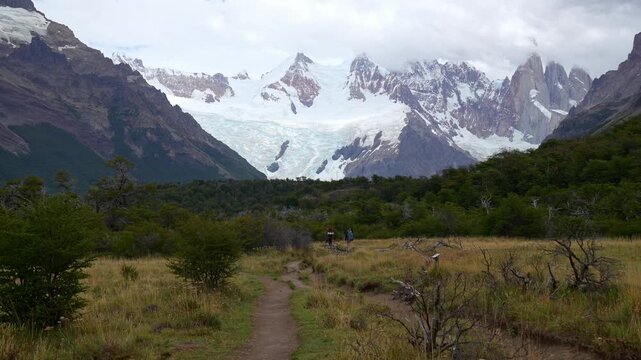 Hikers trekking on a trail towards the snowy peaks and glacier of Mount Fitz Roy in Los Glaciares National Park, Patagonia, Argentina