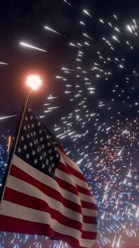 A United States flag waves in the night sky against a backdrop of fireworks