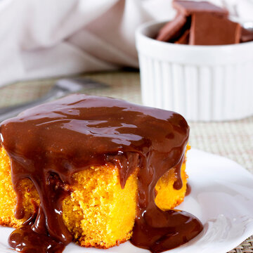 Moist Brazilian carrot cake with a generous creamy chocolate topping on a white plate.