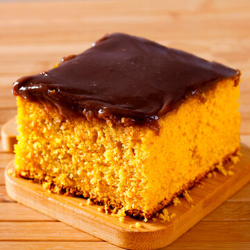 Slice of Brazilian carrot cake with thick chocolate frosting on a wooden board.