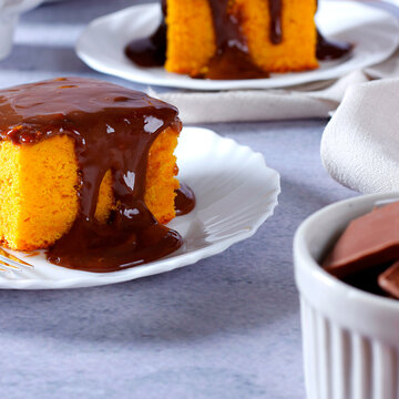 Moist Brazilian carrot cake topped with creamy chocolate, served on a white plate.