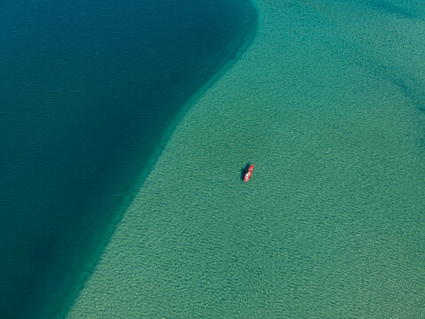 Aerial view of a red kayak paddling in the clear turquoise waters of Dana Point Harbor, transitioning into deep blue ocean depths, Dana Point, California, United States.