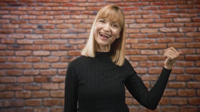 Middle age woman smiling with raised fist and visible face in studio wearing black turtleneck; joyful confidence.