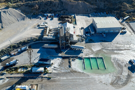 Aerial view of a sand and gravel pit and ready-mix concrete plant with industrial silos, concrete mixing trucks, and turquoise settling ponds in Lehi, Utah, United States.