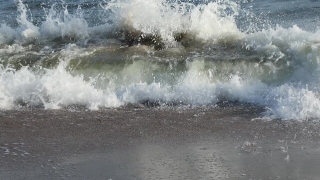 Sea waves with white foam washing over sandy beach. Ocean tide moving along shore. Relaxing coastal nature background, summer vacation and travel concept.