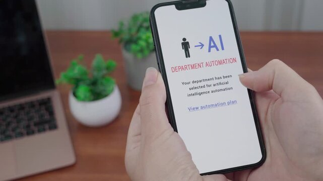 User reads an AI department automation notification on a smartphone above a wooden desk with laptop and plants.