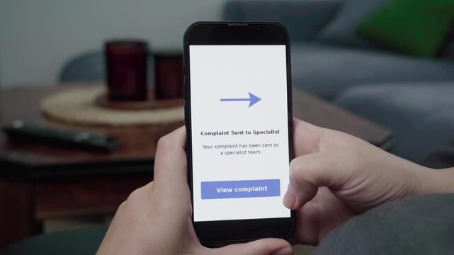 A person checks a Complaint Sent to Specialist message on a phone with a View complaint button in a relaxed home setting.