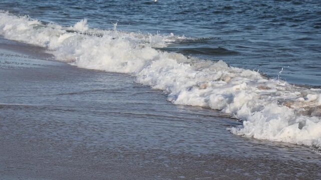 Sea waves with white foam washing over sandy beach. Ocean tide moving along shore. Relaxing coastal nature background, summer vacation and travel concept.