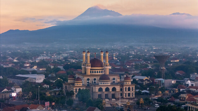 Klaten, Indonesia - 02 July 2026: Aerial view of the Grand Mosque of Klaten surrounded by urban rooftops with the majestic Mount Merapi in the background.