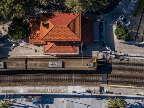 Aerial view of Monte Estoril train station with a train on the tracks, a building with a terracotta roof, and platform area in Estoril, Lisbon, Portugal.