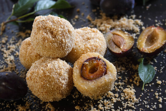 Homemade sweet plum dumplings with breadcrumbs and cinnamon on a black stone background