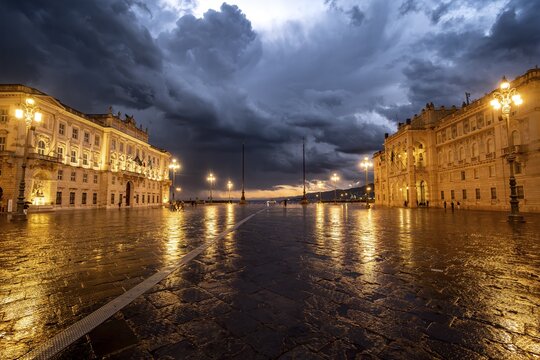 Illuminated square Piazza Unit&agrave; d'Italia, Palazzo del Lloyd Triestino and Palazzo della Luogotenenza Austriaca or Palazzo Governo, with reflection, dramatic clouds, blue hour, old town, Trieste, Friuli-Venezia Giulia region, Italy