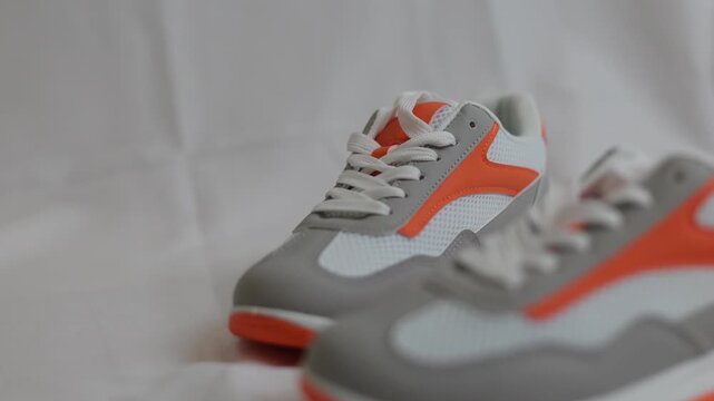 Pair of stylish white and orange sneaker on light background. Modern casual footwear for sport and everyday lifestyle. Fashion trend and comfortable shoe concept for athletic activity