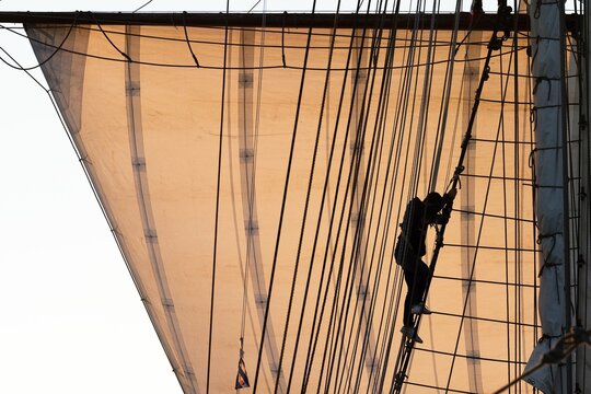 Silhouette of a woman climbing up into the rigging, mainsail backlit, Kongsfjorden, Svalbard archipelago, Svalbard, Norway