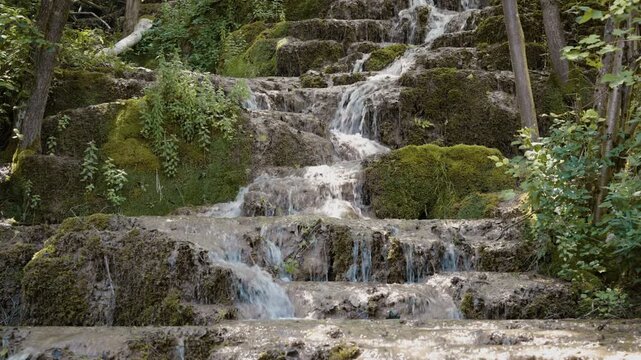 Scenic view of Bigar waterfall cascading over mossy tufa rock steps in a dense forest near Kalna, Stara Planina, Serbia. Cinematic pure nature stream footage shot in summer.