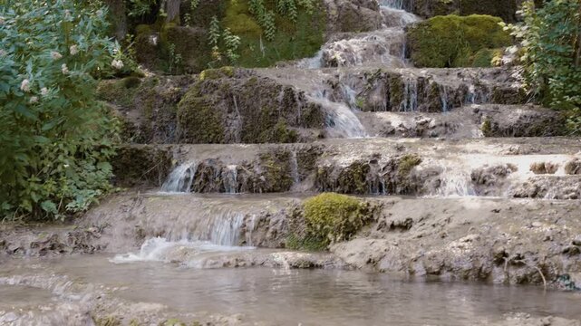 Scenic view of Bigar waterfall cascading over mossy tufa rock steps in a dense forest near Kalna, Stara Planina, Serbia. Cinematic pure nature stream footage shot in summer.