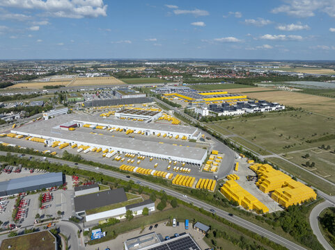 Aschheim, Bavaria, Germany - 20 July 2026: Aerial view of DHL Paketzentrum Aschheim, featuring yellow delivery trucks at the logistics facility, surrounded by industrial buildings and fields.