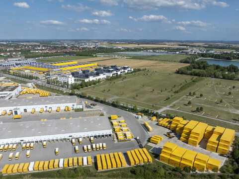 Aschheim, Germany - 20 July 2026: Aerial view of DHL Paketzentrum Aschheim, featuring large industrial warehouses, yellow delivery trucks, and shipping containers in a logistics hub.
