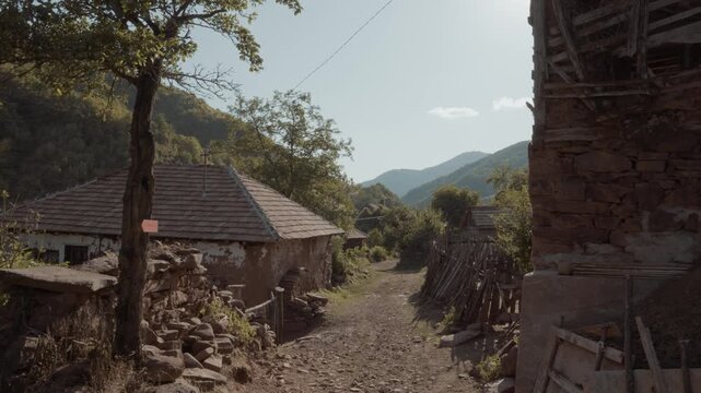 Narrow dirt street view leading through traditional old mud houses, stone walls, and wooden fences in Topli Do village, Stara Planina, Serbia. Rustic Balkan mountain village pathway.