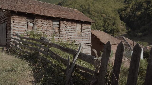Camera moving along a rustic wooden picket fence towards traditional old mud brick houses with clay tile roofs in Topli Do village, Stara Planina, Serbia. Authentic Balkan village scene.
