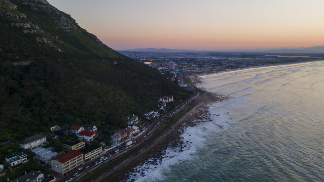 Cape Town, Western Cape, South Africa - 17 August 2026: Aerial view of Muizenberg coastline with houses along the mountain slopes at sunset and waves crashing on the shore.