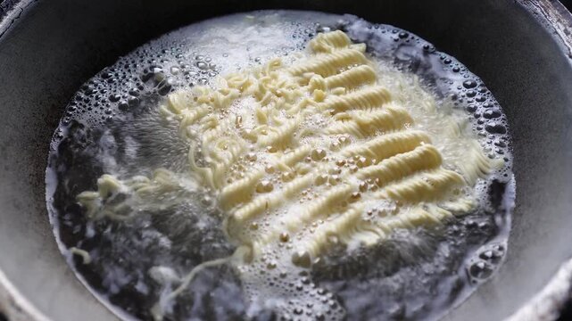 Close-up of instant noodles cooking in boiling water inside a pot. Steam rises as noodles soften. Simple, authentic food preparation scene for culinary or convenience meal concepts.