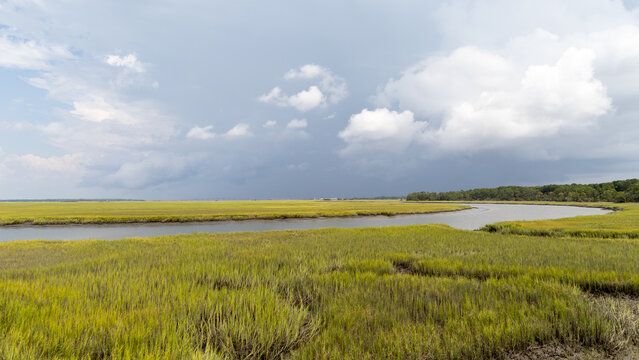 Drone view of marshland with waterway under cloudy sky at midday