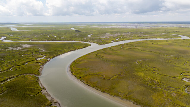 Drone view of winding river through green landscape in coastal area during daylight