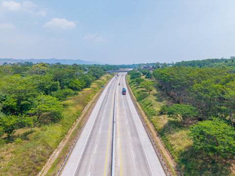 Aerial view of a multi-lane highway stretching through a lush green forested landscape in Indonesia.