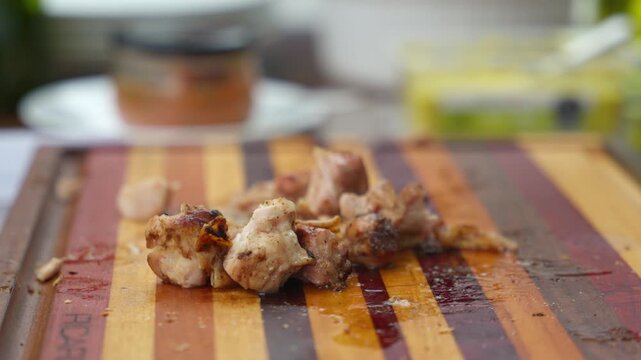 Hand picking grilled meat cubes from wooden board