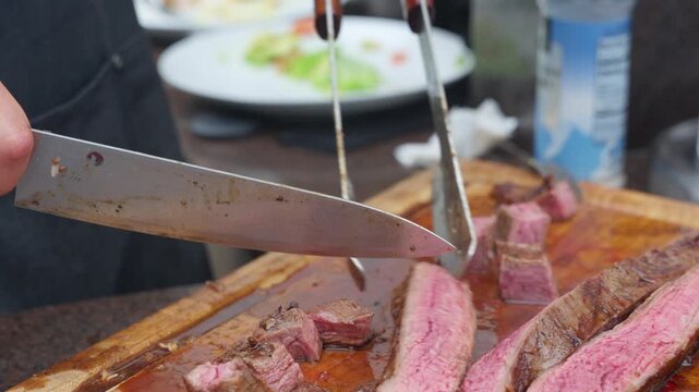 Chef slicing juicy grilled beef steak on a wooden board