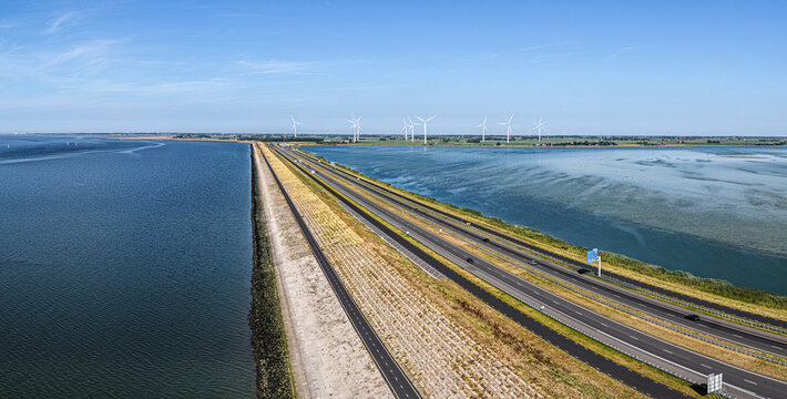 Aerial view of the Afsluitdijk causeway separating the Wadden Sea and IJsselmeer, featuring a highway, wind turbines, and coastal landscape in Breezanddijk, Friesland, Netherlands.