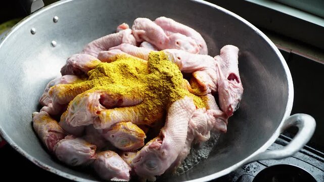 Raw chicken pieces seasoned with vibrant yellow spice in a metal wok ready for cooking. Authentic culinary preparation captured in natural kitchen lighting, elegantly showcasing food.