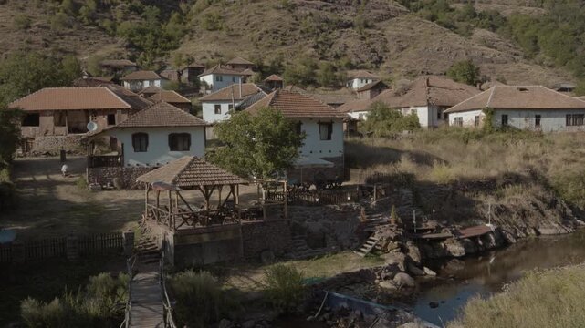 Panoramic view of authentic rural houses with red tile roofs alongside a small river in Topli Do village, Stara Planina, Serbia. Cinematic shot of traditional Balkan mountain village.