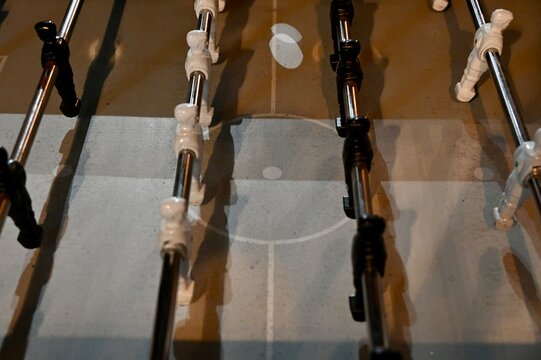 A side-angle perspective shot of a foosball table featuring black and white plastic figures mounted on metallic rods, ideal for concepts of sport, entertainment, teamwork, and leisure activities.