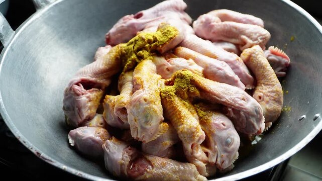 Raw chicken pieces seasoned with vibrant yellow spice in a large metal wok ready for cooking. Close-up shot highlights texture and color contrast of ingredients.