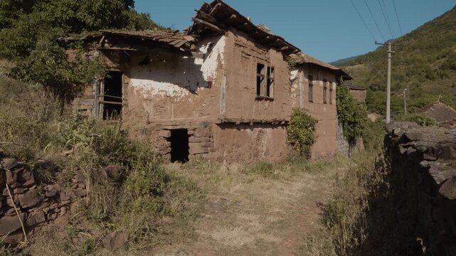 Camera panning left to right showing old abandoned traditional mud brick and wooden houses in Topli Do village, Stara Planina, Serbia. Cinematic shot of Balkan authentic rural heritage.