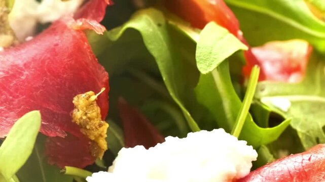 Fresh gourmet salad with sliced bresaola, creamy cheese, pesto, and arugula leaves macro close up