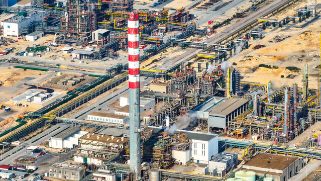 Aerial view of a large industrial oil refinery complex featuring a tall red-and-white striped chimney, intricate pipe networks, and storage tanks in Sines, Setubal, Portugal.