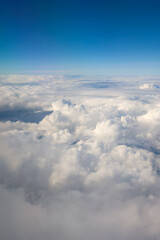 Fototapeta premium White fluffy cumulus clouds extend to the horizon under a clear blue sky, forming a serene cloudscape from an aerial perspective
