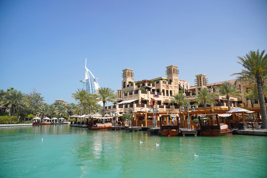 Aerial view of Souk Madinat Jumeirah with traditional wooden boats on the water and the Burj Al Arab in the background under a clear blue sky in Dubai, Dubai, United Arab Emirates.