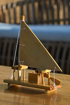 miniature wooden sailboat model on wooden table, handcrafted wooden jangada boat craft at seaside outdoor lounge, rustic nautical decor for tropical event close up