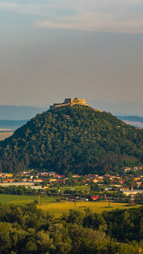 Aerial view of Deva Fortress situated on a forested hill overlooking the town with surrounding fields and meadows in Deva, Hunedoara, Romania.