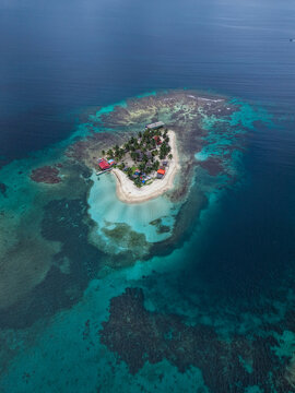 Aerial view of a small tropical island with palm trees, white sand beaches, and vibrant coral reefs surrounded by turquoise waters in Guna Yala Comarca, Panama.